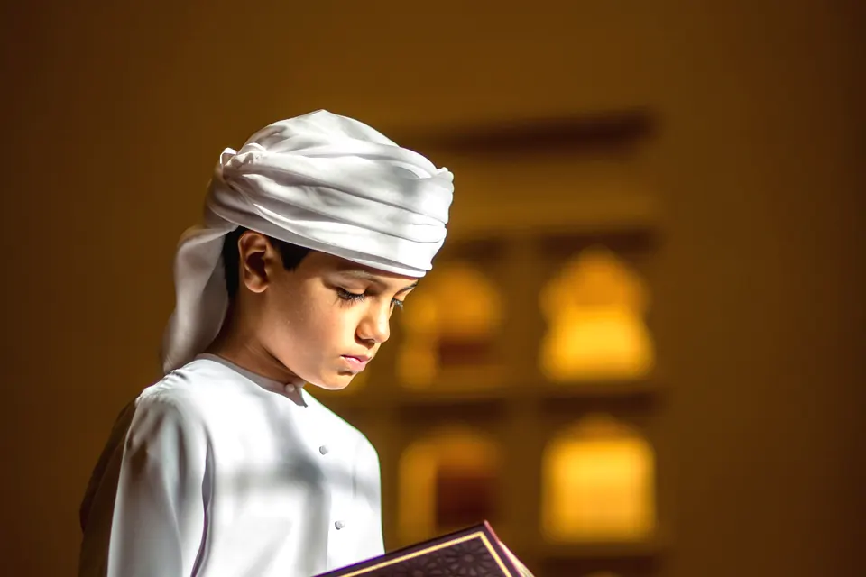 A boy in traditional dress reciting from the Quran in a quiet mosque