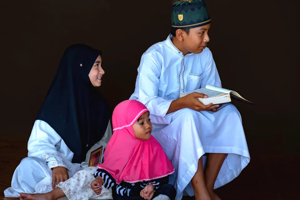 Children in modest dress sitting together with a Quran during a lesson
