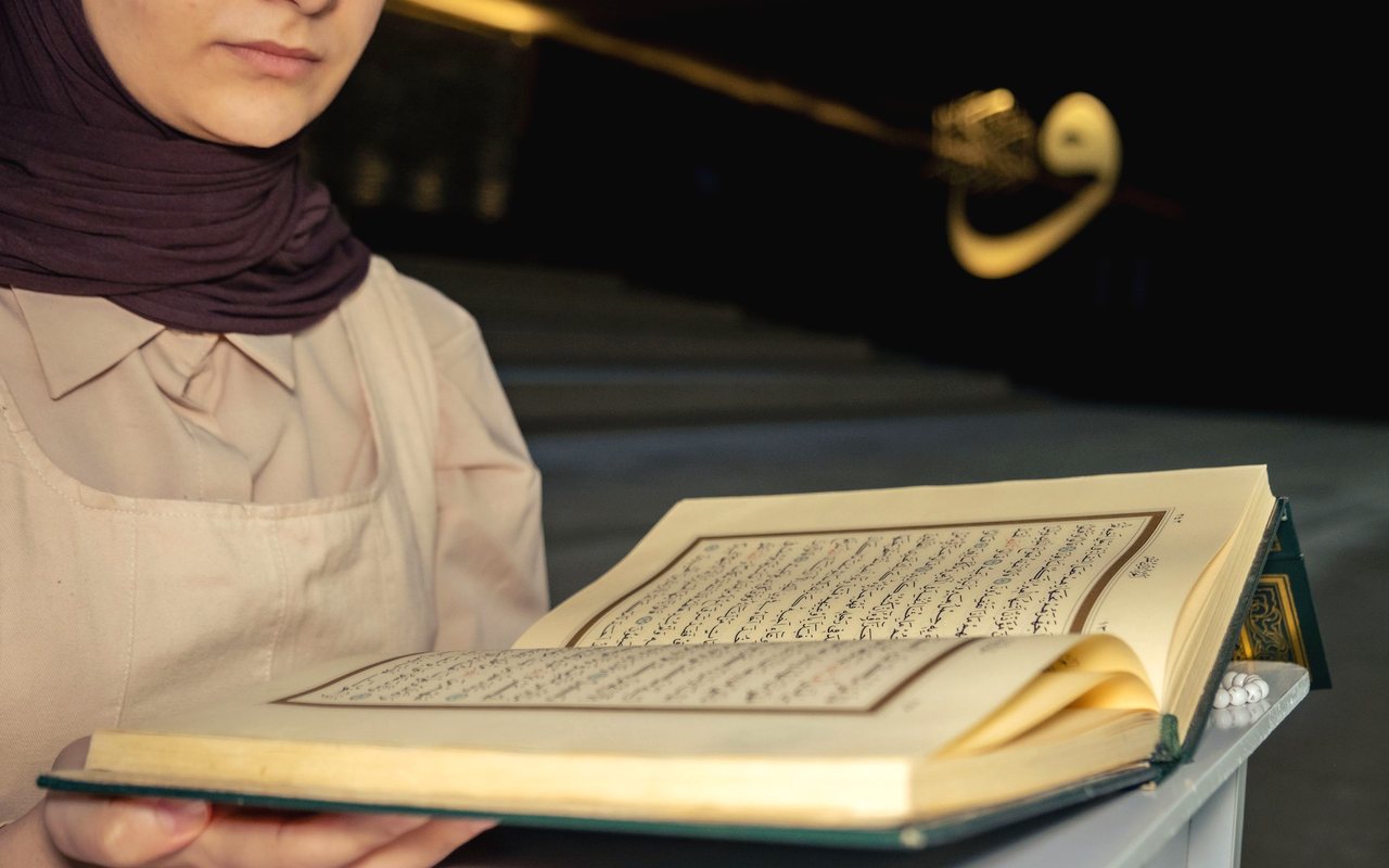 A woman in a hijab reading from an open Quran