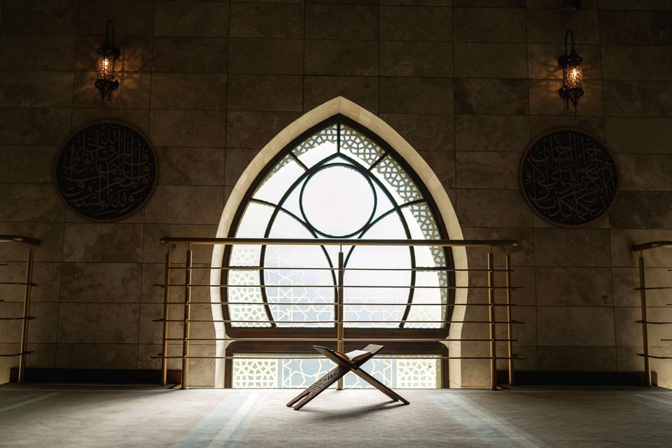 A wooden Quran stand in front of a pointed mosque window